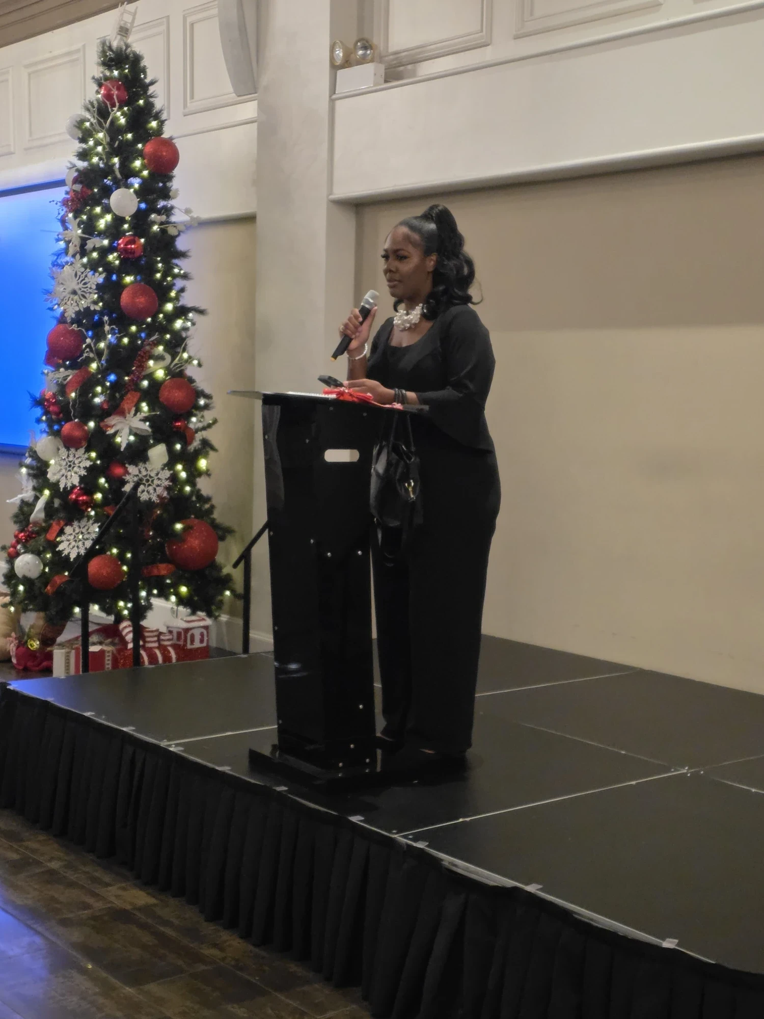 The host speaking at the podium beside the Christmas tree